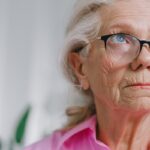 At-Home Care Can Help Seniors Age Joyfully an elderly woman wearing glasses and a pink shirt gazing off in the distance
