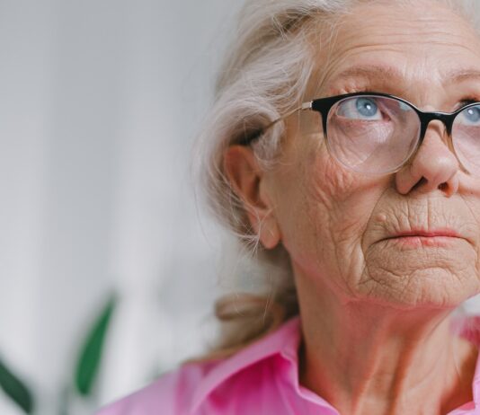 an elderly woman wearing glasses and a pink shirt gazing off in the distance