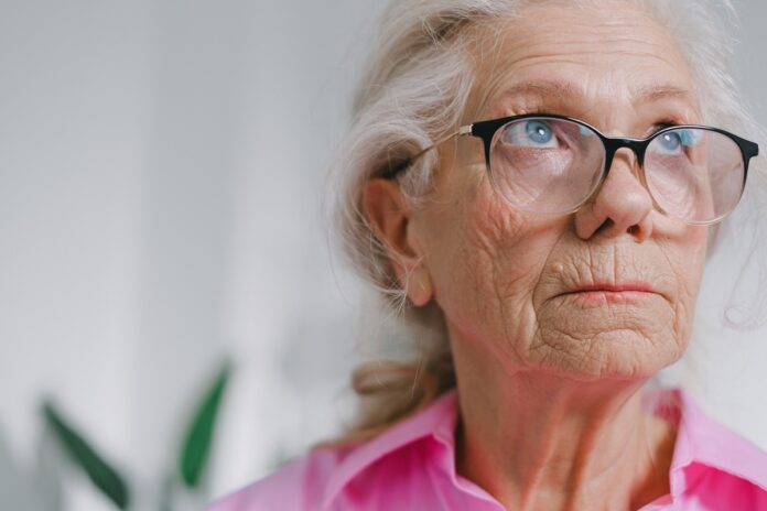 an elderly woman wearing glasses and a pink shirt gazing off in the distance
