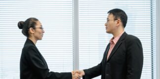 The head of a nonprofit wearing a long black coat shakes hands with a top donor in her office