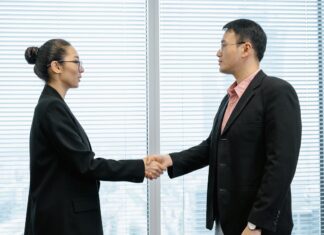 The head of a nonprofit wearing a long black coat shakes hands with a top donor in her office