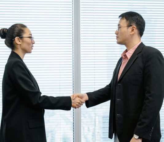 The head of a nonprofit wearing a long black coat shakes hands with a top donor in her office
