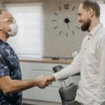 A man in a white shirt shakes hands with a dental hygienist in an examination room