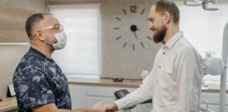 A man in a white shirt shakes hands with a dental hygienist in an examination room