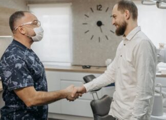 A man in a white shirt shakes hands with a dental hygienist in an examination room