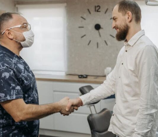 A man in a white shirt shakes hands with a dental hygienist in an examination room